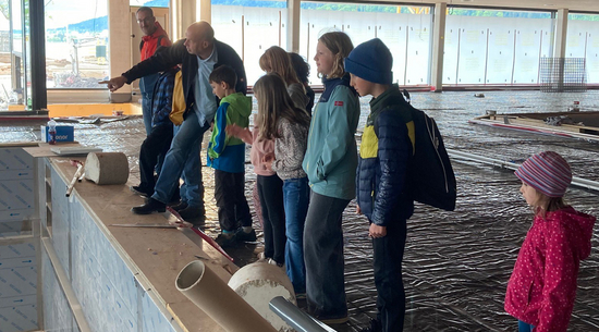 Das Bild zeigt eine Baustellenbegehung des neuen Seebades in Bregenz mit Kindern. Projektleiter Bernd Raica zeigt den Kinderreportern ein neues Innenbecken auf der Baustelle.