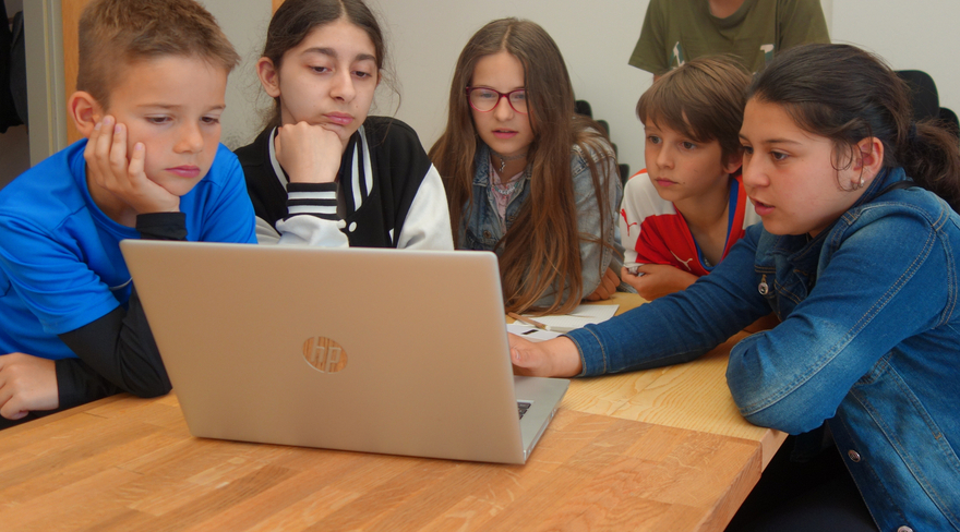 Diese Abbildung zeigt sechs Kinder, welche gemeinsam an einem Tisch sitzen und in einen Laptop schauen.