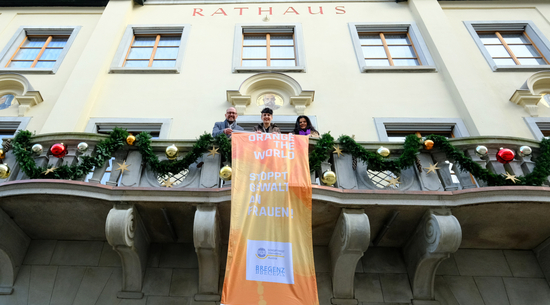 Diese Abbildung zeigt Bürgermeister Michael Ritsch und Vizebürgermeisterin Sandra Schoch und eine Mitarbeiterin des Frauenservice auf dem Balkon des Rathauses. Sie halten eine Flagge, auf welcher "Orange the World - Stoppt Gewalt an Frauen" steht.