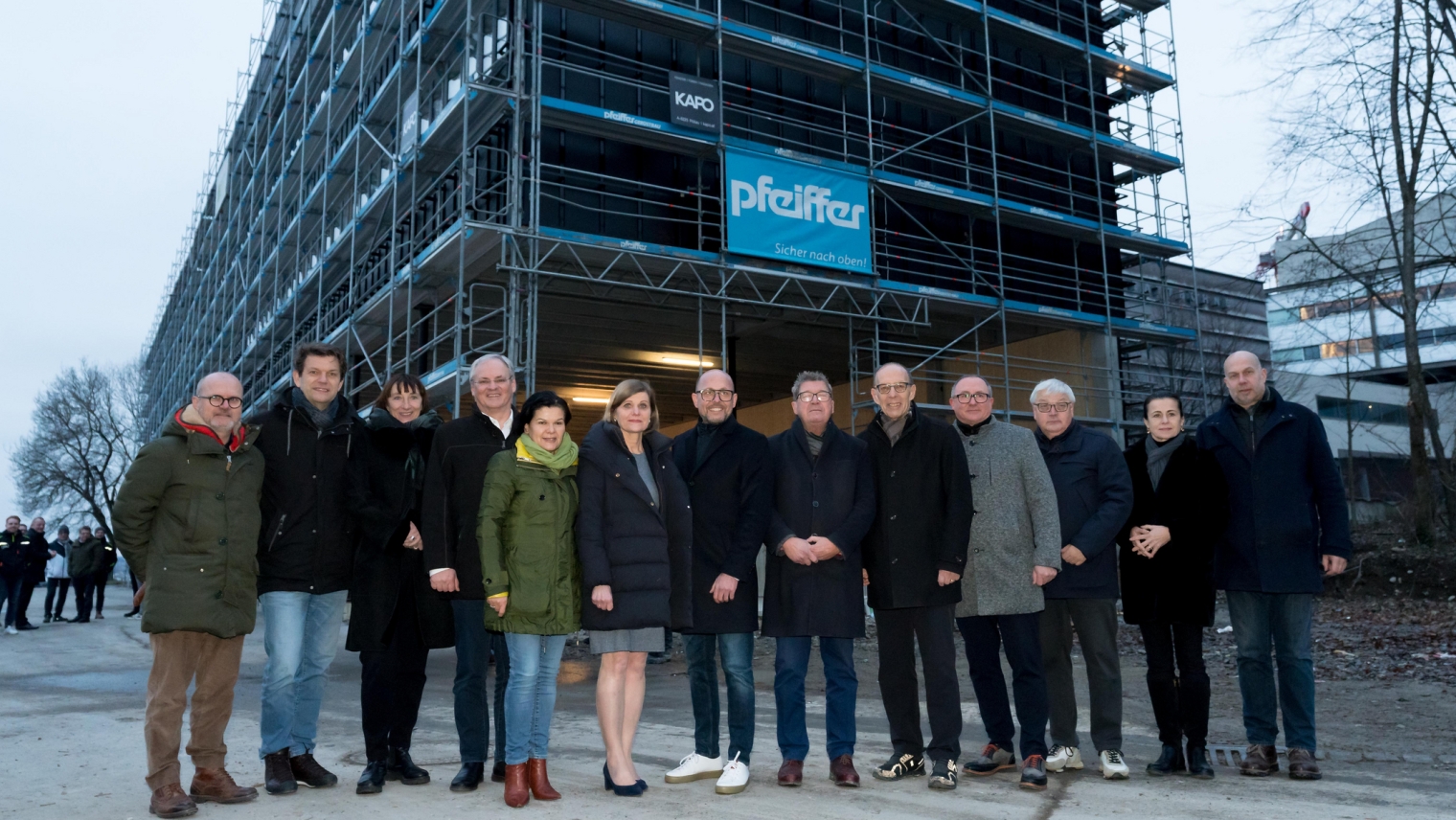 Diese Abbildung zeigt Bürgermeister Michael Ritsch mit einigen anderen Personen vor dem neuen Mehrzweckgebäude, welches eingerüstet ist.