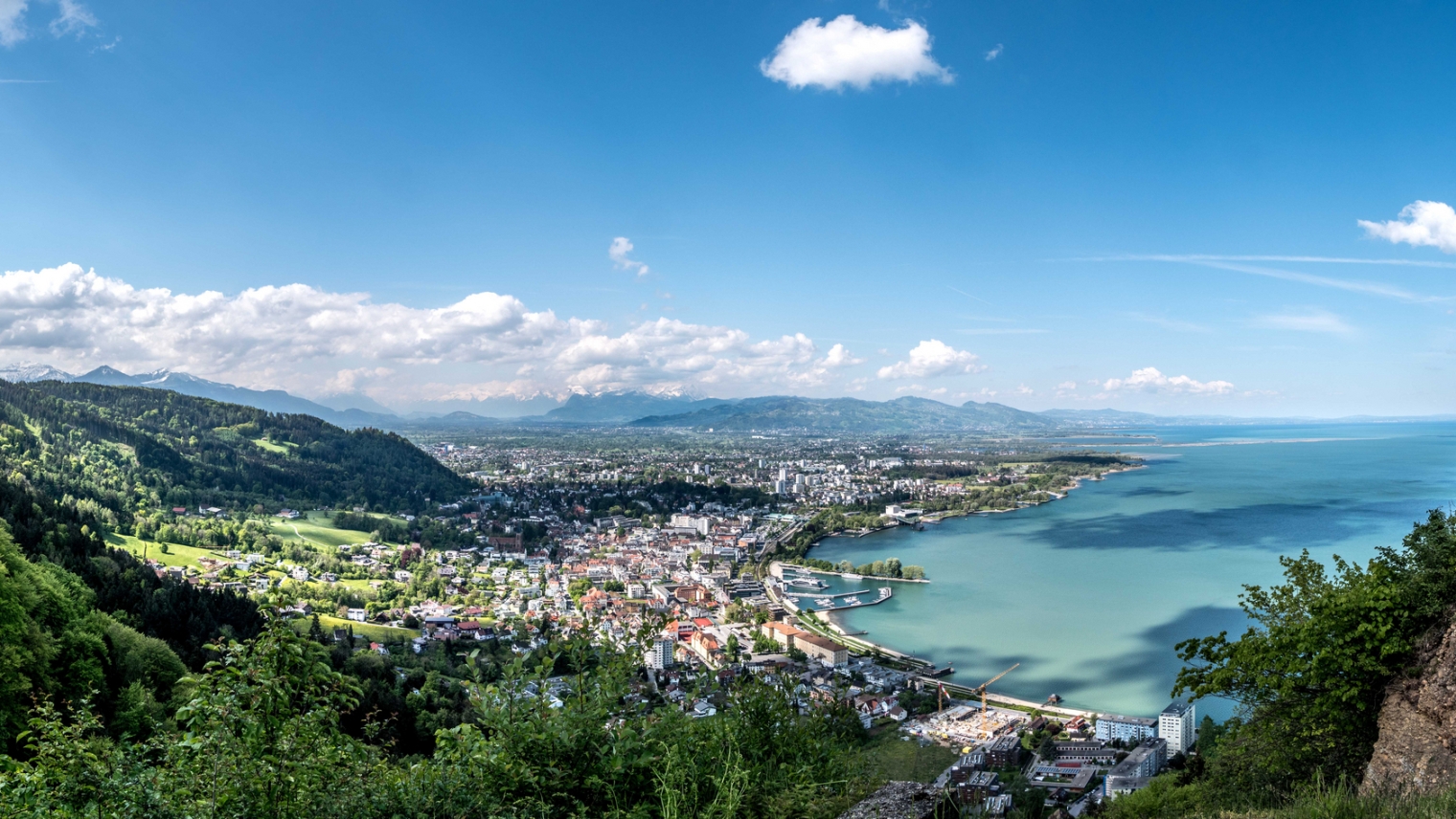 Auf dem Bild ist ein Panorama von Bregenz von oben zu sehen. Der Himmel ist blau.