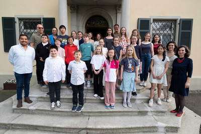 Das Bild zeigt die Gewinner:innen des "prima la musica"-Landeswettbewerbes, die alle zusammen vor der Eingangstüre der Musikschule Bregenz auf den Treppen aufgereiht sind und in die Kamera blicken.