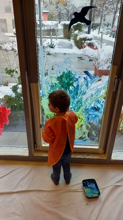 Auf dem Bild ist ein Kleinkind beim Bemalen eines Fensters zu sehen. 