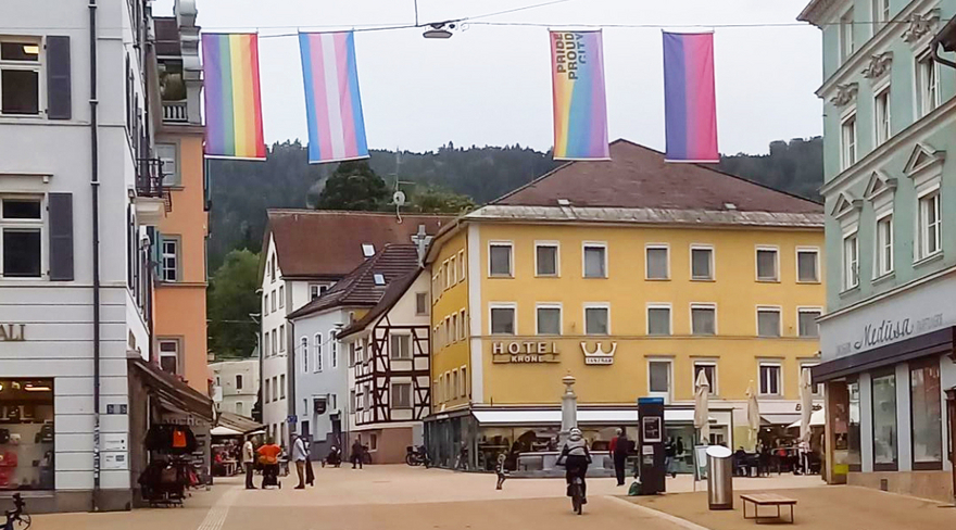 Das Bild zeigt vier LGBTIQ+ Fahnen, die in der Bregenzer Innenstadt über der Straße aufgehängt sind. 