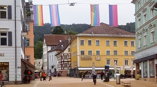 Das Bild zeigt vier LGBTIQ+ Fahnen, die in der Bregenzer Innenstadt über der Straße aufgehängt sind. 