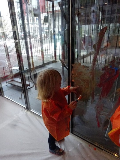 Auf dem Bild ist ein Kleinkind beim Bemalen eines Fensters zu sehen. 