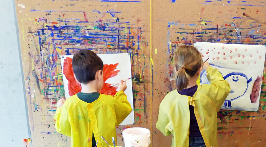 Hier wurden Kinder, welche am malen sind, fotografiert. Alle tragen einen gelben Mantel.
