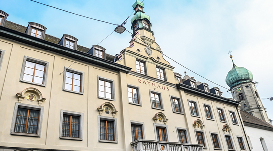 Das Bild zeigt das Bregenzer Rathaus von außen vor blauem Himmel. Auf der Gebäudefassade ist die Aufschrift "Rathaus" gut zu lesen. 