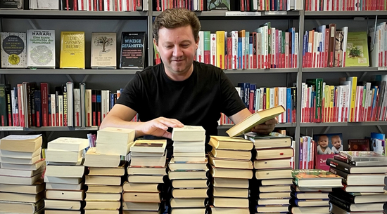Diese Abbildung zeigt einen Mann, welcher von Büchern umgeben ist.