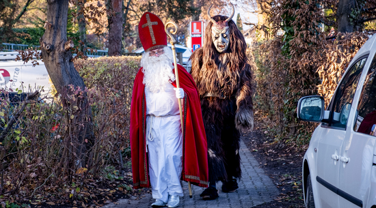 Das Bild zeigt einen Nikolaus im klassischen Kostüm links und rechts einen Knecht Ruprecht, ebenfalls im klassischen Kostüm, die eine Straße entlanglaufen.