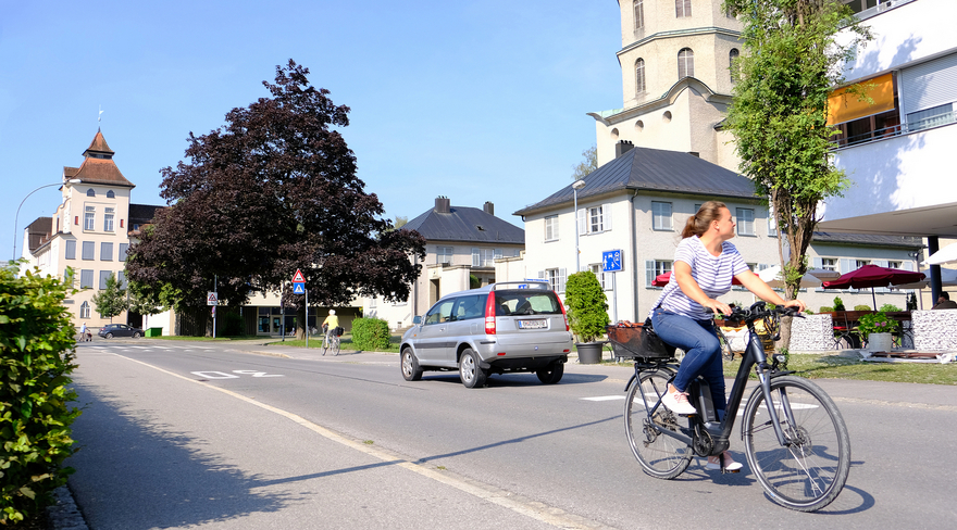 Das Bild zeigt die Mariahilfstraße in Bregenz mit einer Radfahrerin und einem Auto.