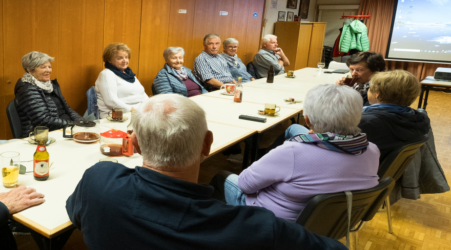 Das Bild zeigt mehrere Senior:innen, die um einen Tisch sitzen und sich unterhalten.