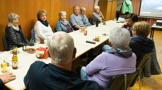 Das Bild zeigt mehrere Senior:innen, die um einen Tisch sitzen und sich unterhalten.