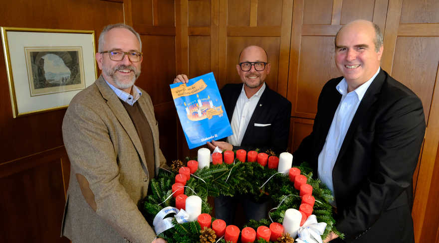 In dieser Abbildung ist der Bürgermeister Michael Ritsch mit zwei weiteren Männern zu sehen, wie sie einen Adventkranz auf den Händen tragen.
