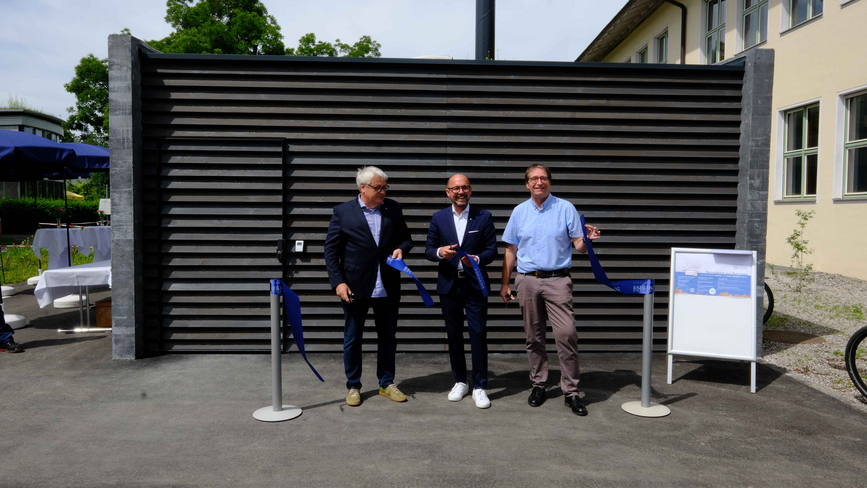 Diese Abbildung zeigt Bürgermeister Michael Ritsch mit zwei weiteren Personen, welche vor dem neuen Biomasse-Heizkraftwerk in Rieden stehen und eine blaue Schleife durchschneiden.