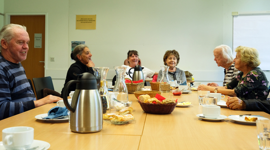 Mehrere Senior:innen sitzen beim Dienstagsfrühstück an einem Tisch und frühstücken zusammen, während sie Gespräche führen. 
