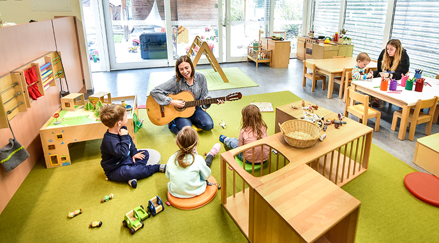 Das Bild zeigt eine Pädagogin bei der Musikerziehung mit Kleinkindern in der Kinderbetreuungseinrichtung Schöllersteig.